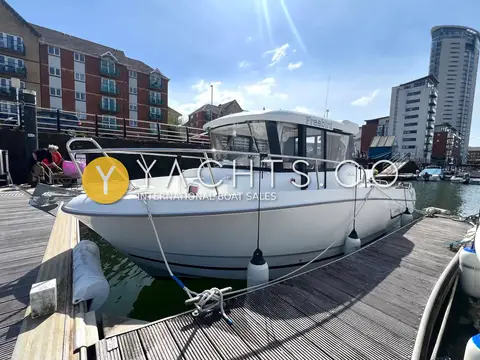 Jeanneau Merry Fisher 755 Marlin: starboard bow quarter alongside a pontoon with waterside apartment buildings behind
