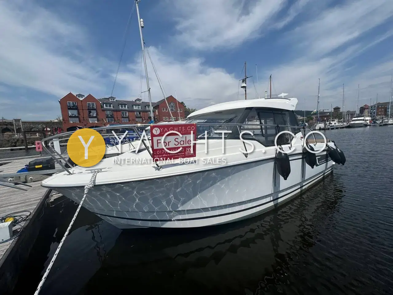 Jeanneau Merry Fisher 795: white pilothouse motor boat moored stern-on at a marina pontoon beside brick apartment buildings