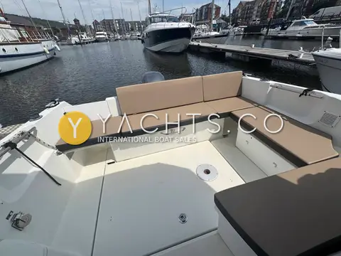 Jeanneau Merry Fisher 795: aft cockpit bench with beige cushions wrapping around the transom, marina behind