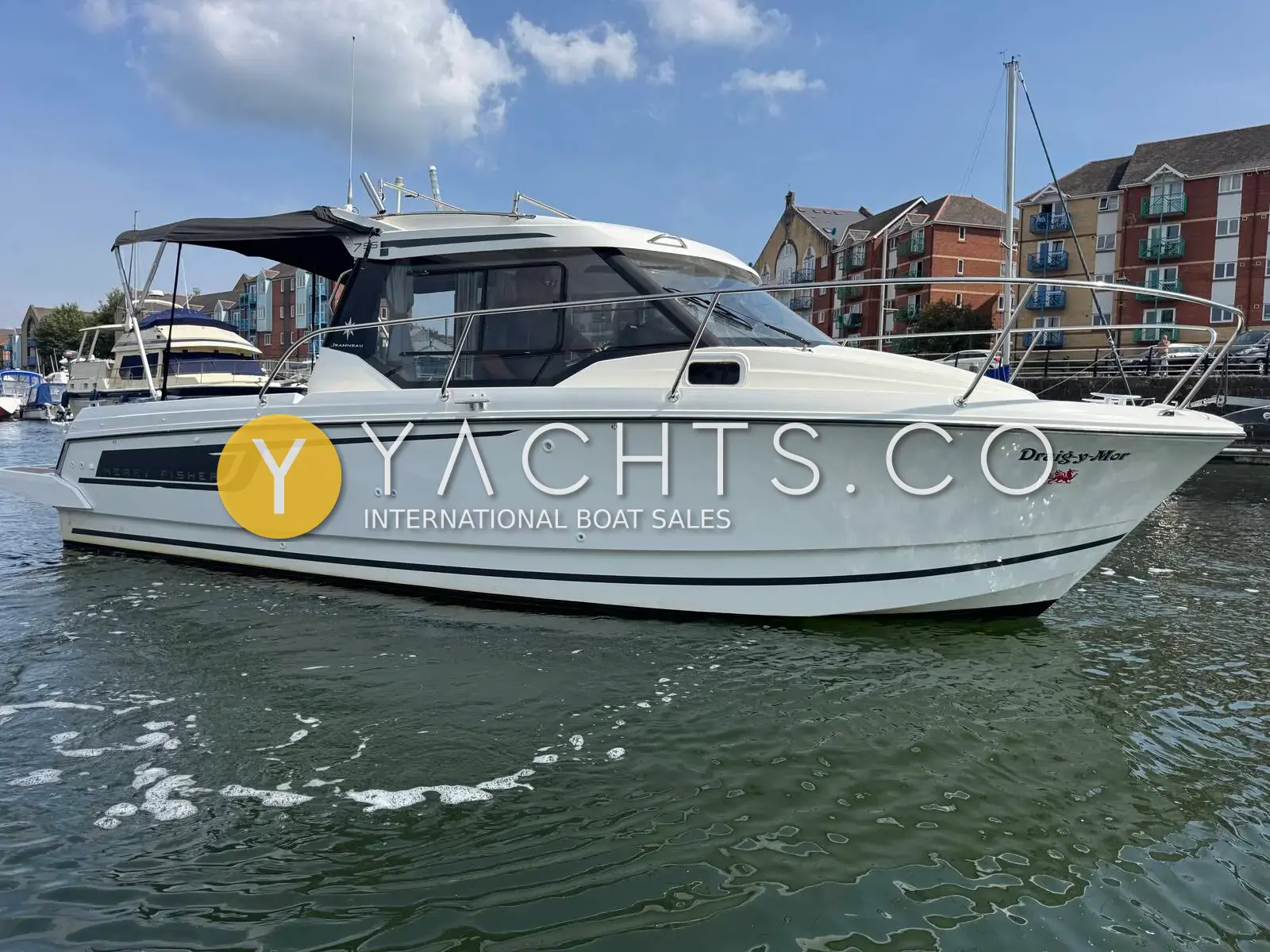 Jeanneau Merry Fisher 795: starboard side of the white wheelhouse cruiser moored in a marina with flats behind