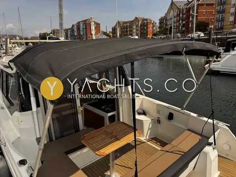 Jeanneau Merry Fisher 795: cockpit under grey canopy with folding table and teak-effect deck