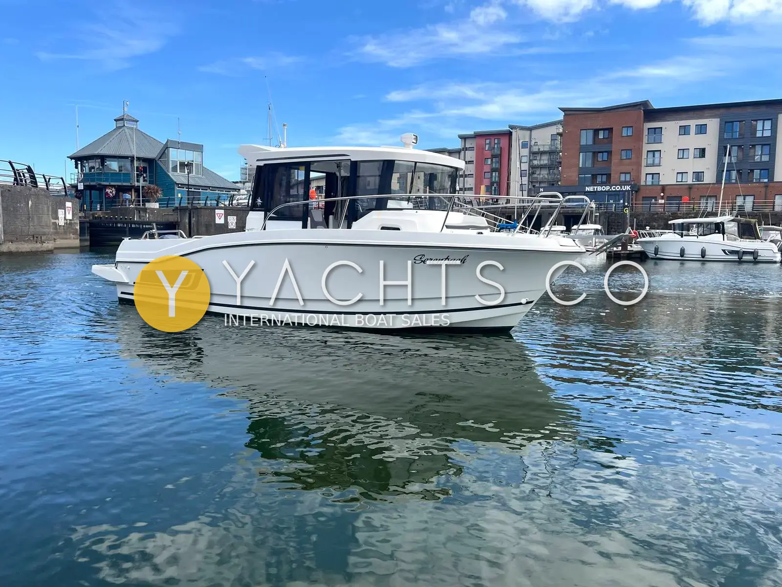 Jeanneau Merry Fisher 795 Marlin: starboard side of white pilothouse hull afloat in a marina beside a turreted harbour building