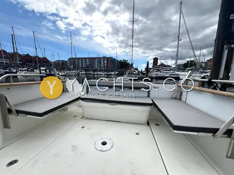Jeanneau Merry Fisher 795 Marlin: aft cockpit with U-shaped grey cushioned seating and central bench, marina behind