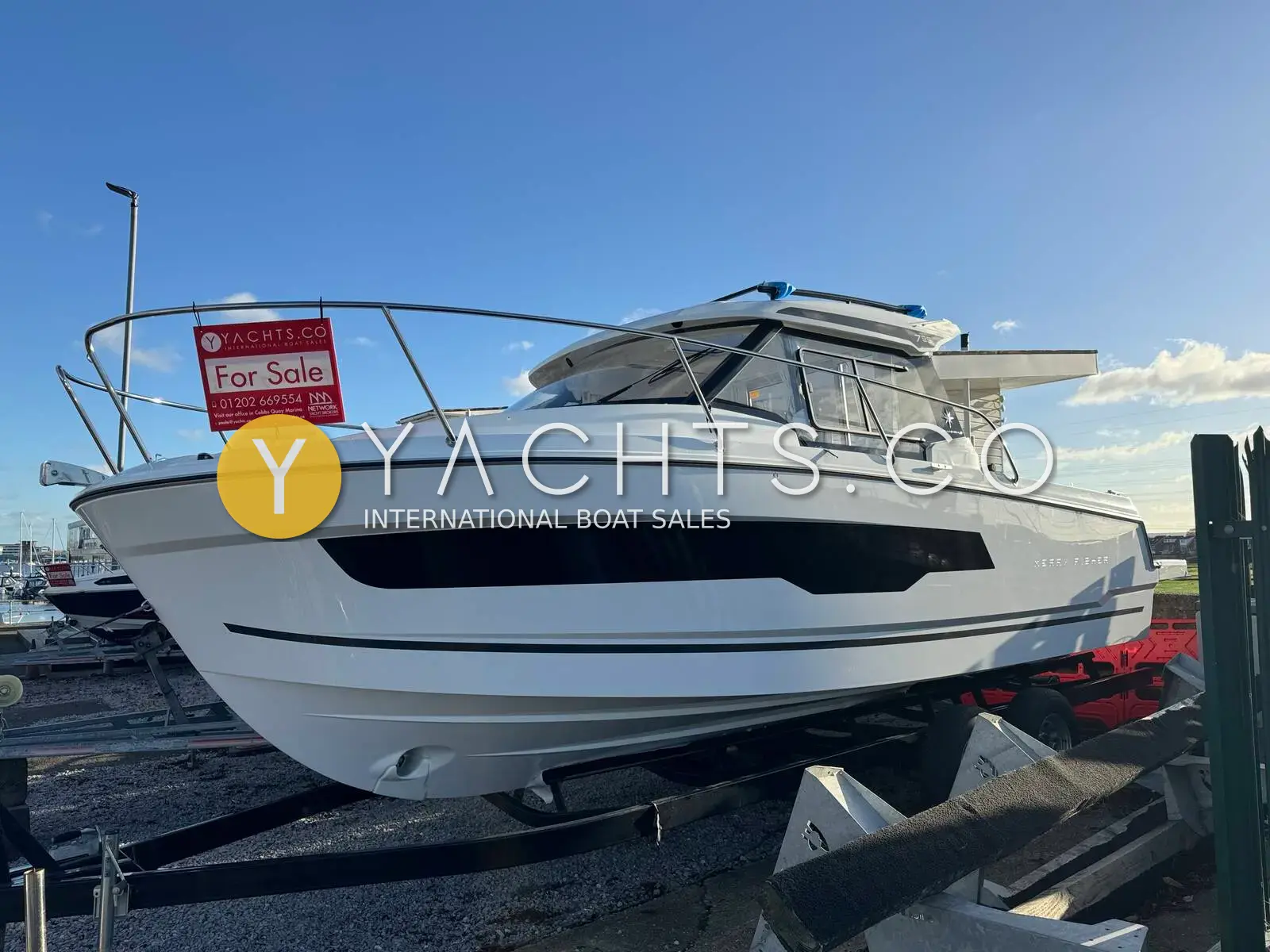 Jeanneau Merry Fisher 795 S2: white hull ashore on blocks in a boatyard under blue sky, wheelhouse and guardrails visible