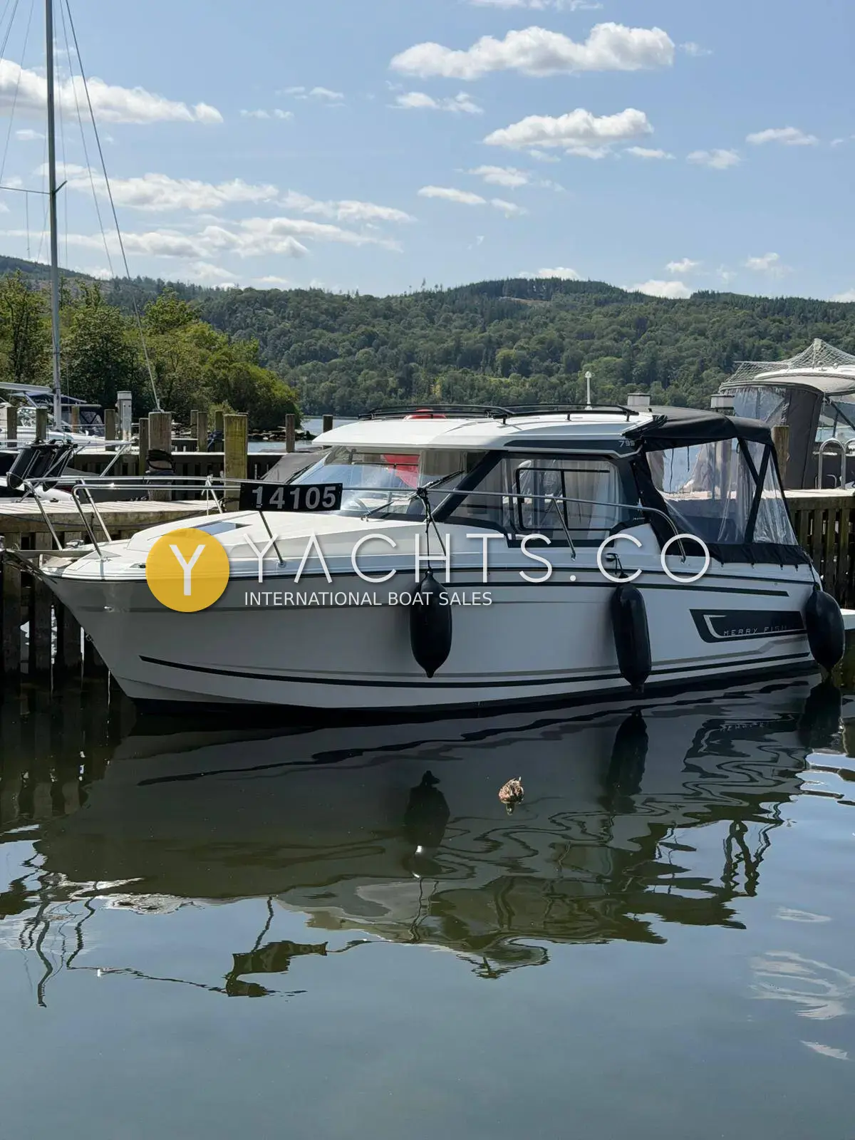 Jeanneau Merry Fisher 795 S2: white hull with dark wheelhouse canopy moored at a wooden pontoon with wooded hills behind