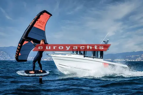 Jeanneau Merry Fisher 795 Sport: under way at speed on blue water with a wing foiler riding alongside