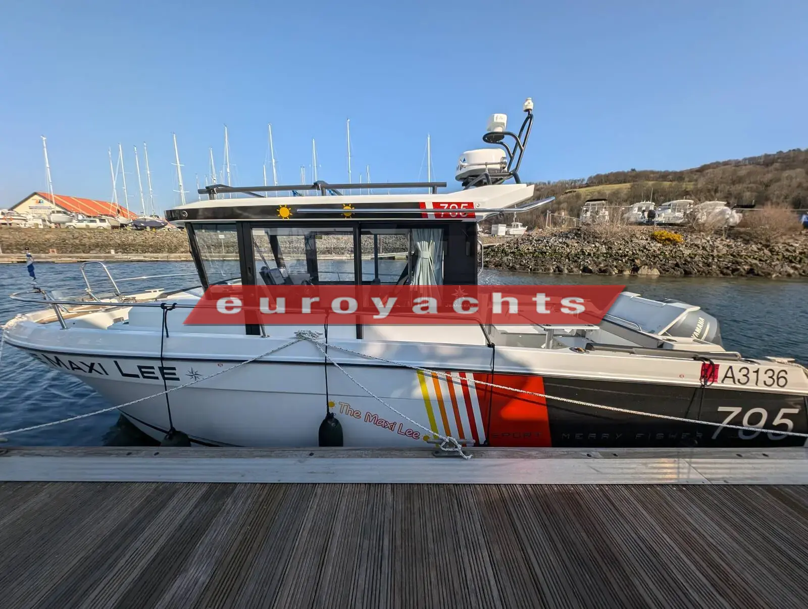 Jeanneau Merry Fisher 795 Sport S2: starboard side of the white hull with red and yellow stripes, moored at a pontoon