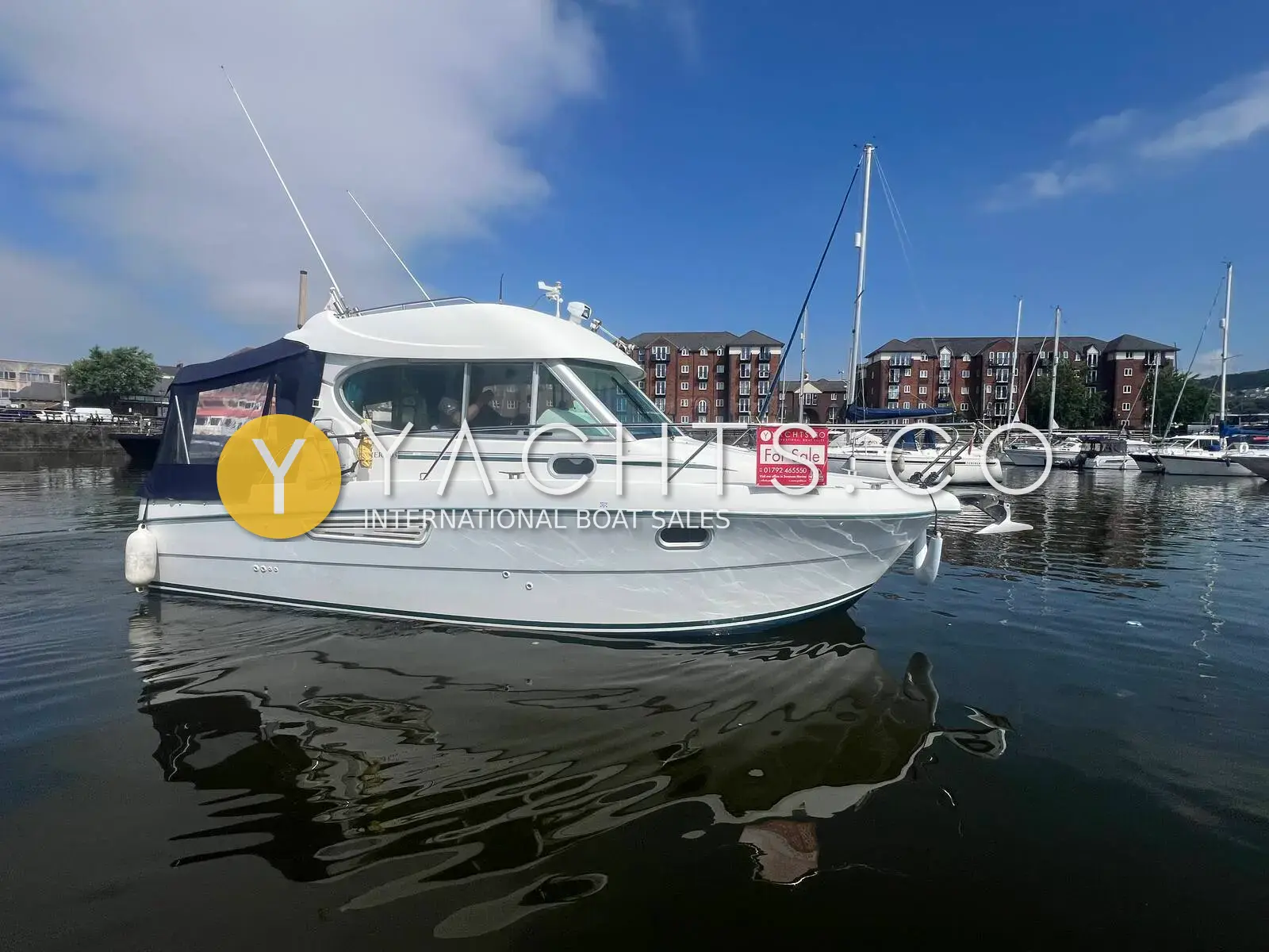 Jeanneau Merry Fisher 805: white hull with dark blue cockpit canopy, afloat in a marina with flats behind