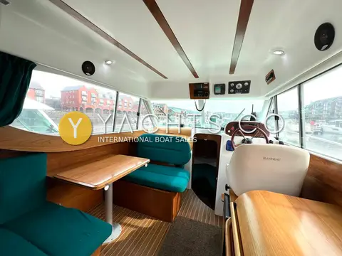 Jeanneau Merry Fisher 805: wheelhouse saloon with green dinette to port, wooden table and helm seat forward