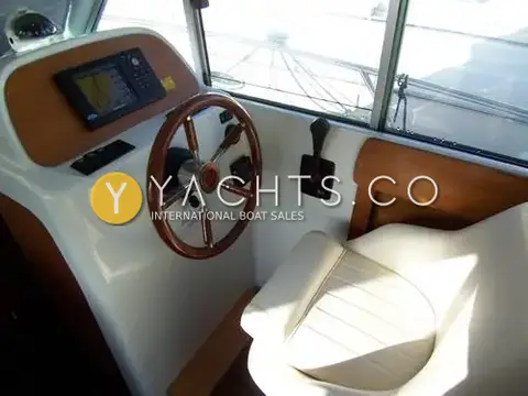 Jeanneau Merry Fisher 805: helm station with wooden wheel, chartplotter in a wood panel, throttle and cream seat