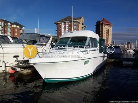 Jeanneau Merry Fisher 805: bow quarter view of white hull with green boot stripe, moored beside marina apartments