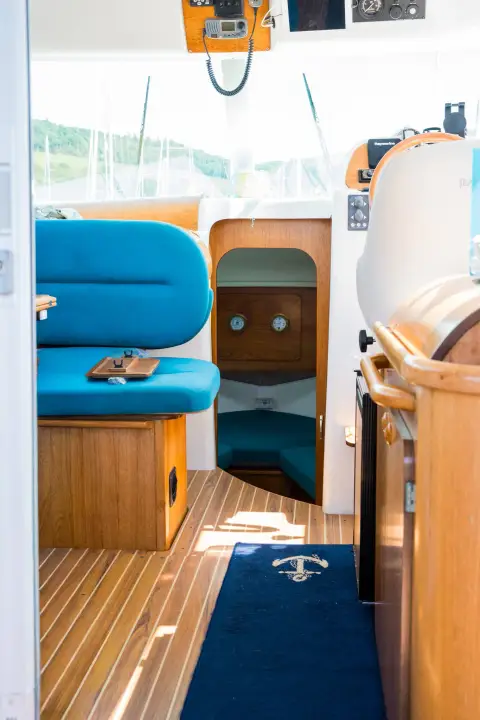 Jeanneau Merry Fisher 805: saloon walkway past blue seat and galley towards the forward cabin, with anchor-motif floor mat