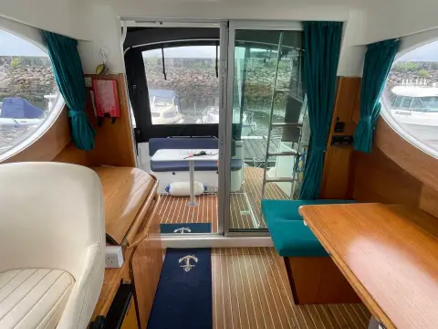 Jeanneau Merry Fisher 805: saloon looking aft to sliding glass door, teal curtains and the enclosed cockpit beyond