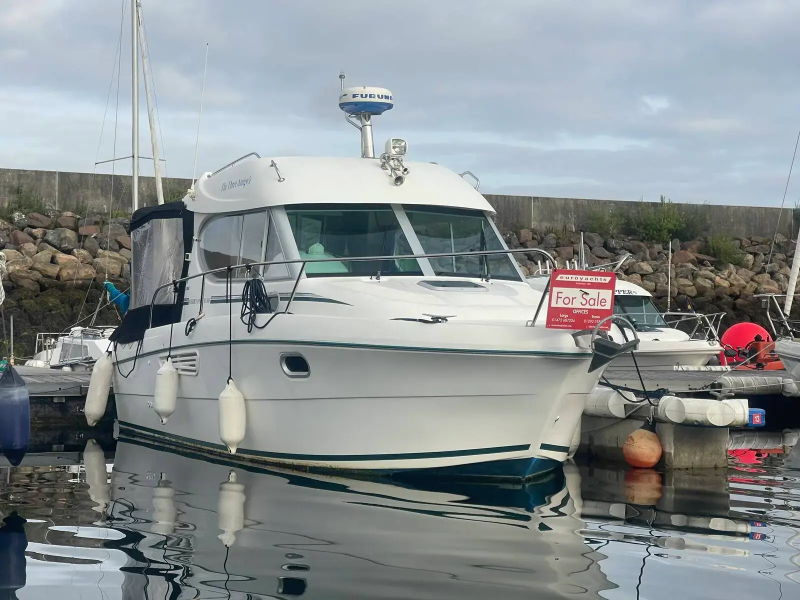 Jeanneau Merry Fisher 805: white hull and wheelhouse afloat in a marina berth with fenders out and a harbour wall behind
