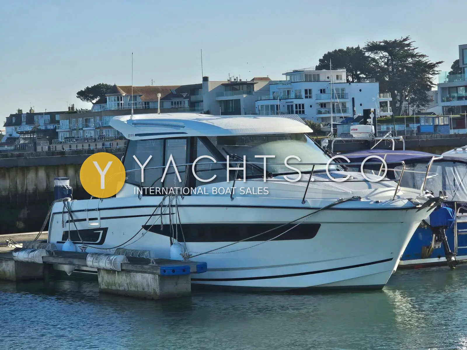 Jeanneau Merry Fisher 895: starboard side of the white hull and wheelhouse moored at a pontoon with waterfront buildings behind