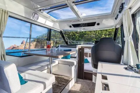Jeanneau Merry Fisher 895 S2: bright wheelhouse saloon with glass roof panels, white upholstery and dinette table