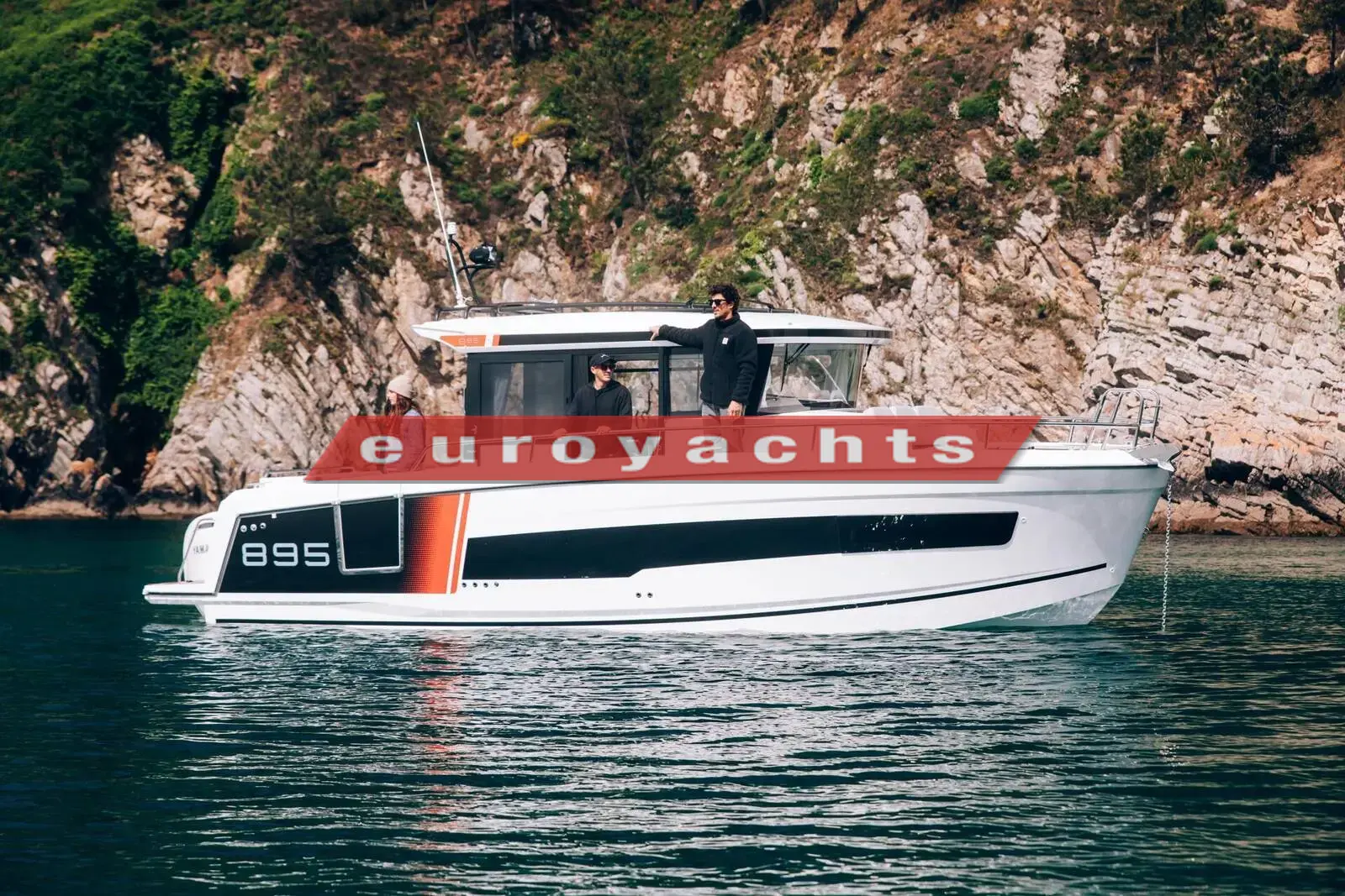 Jeanneau Merry Fisher 895 Sport S2: white hull with black window band underway near a rocky green shoreline