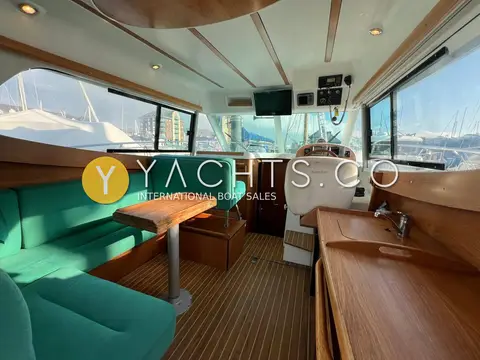 Jeanneau Merry Fisher 925: saloon with green upholstered dinette, wooden table, striped laminate floor and helm seat beyond
