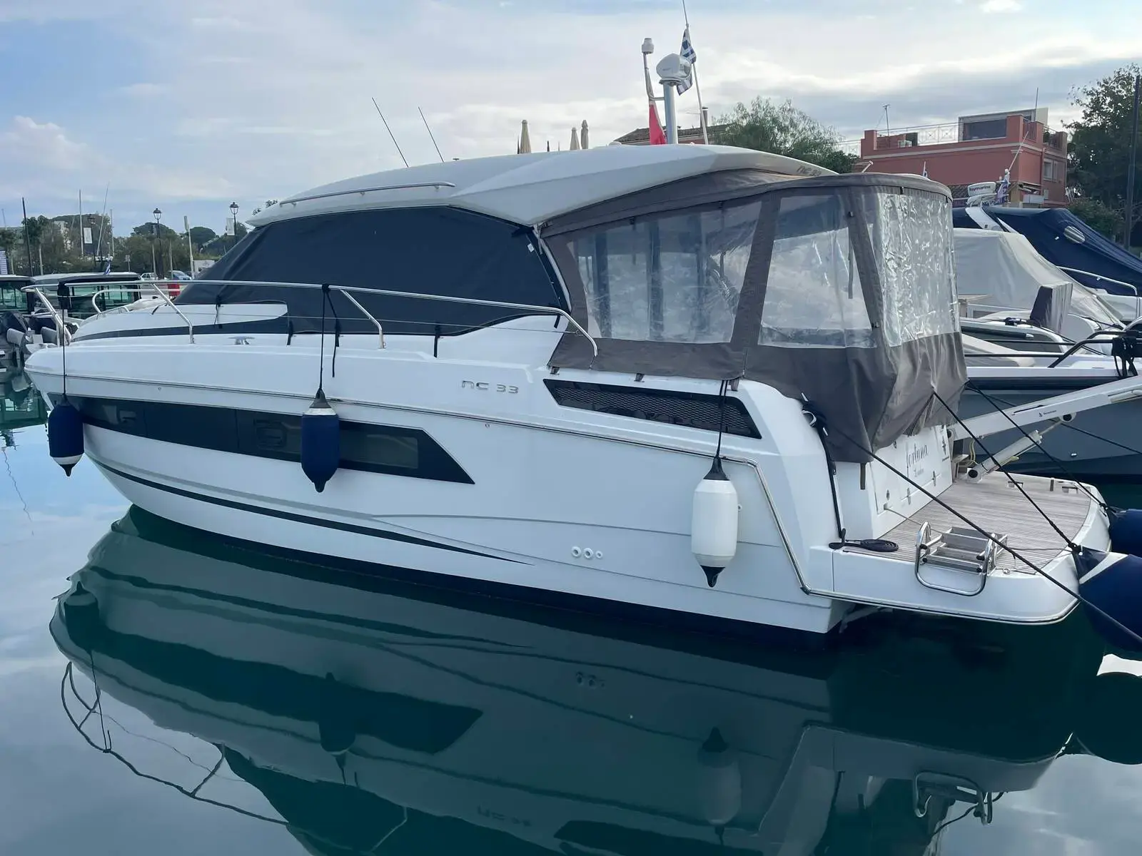 Jeanneau NC 33: white hull with grey hard-top and canvas enclosure, moored stern-to in a marina