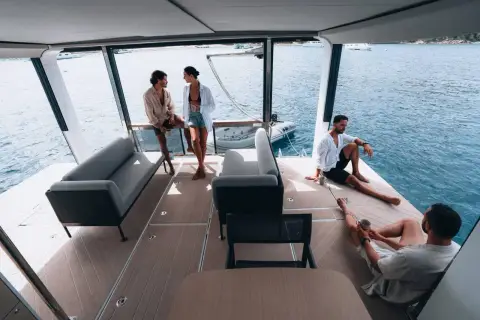 Jeanneau Sea Loft 480: aft lounge with grey sofas and guests relaxing on the open stern deck