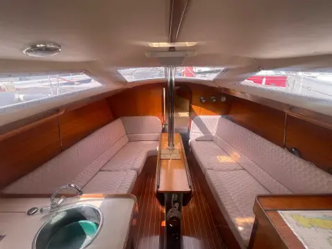 Jeanneau Sun Dream 28: saloon looking forward with teak joinery, grey upholstered settees and folding table