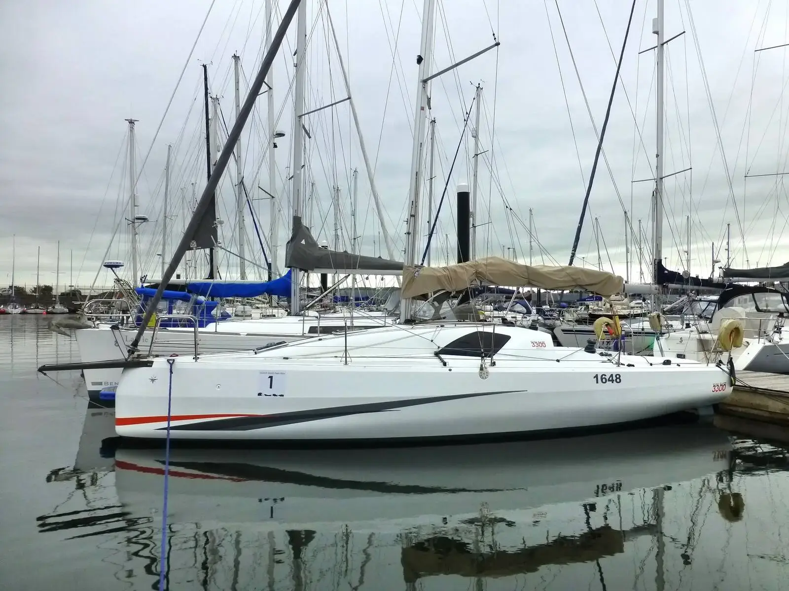 Jeanneau Sun Fast 3300: white hull with red and grey stripes moored in a marina among other yachts