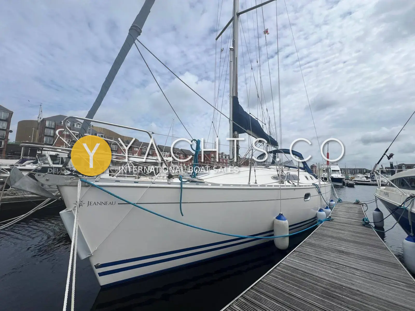 Jeanneau Sun Odyssey 34.2: white hull with blue stripes moored stern-on at a pontoon, brick apartments behind