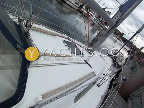 Jeanneau Sun Odyssey 34.2: side deck looking forward past spray hood, with teak handrails, hatch and shrouds in a marina