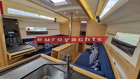 Jeanneau Sun Odyssey 349: saloon with blue cushions, light oak joinery and large hull windows, seen from the galley