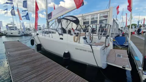 Jeanneau Sun Odyssey 350: white hull alongside a pontoon at a boat show, with sprayhood fitted