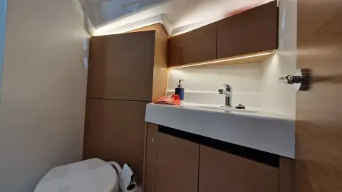 Jeanneau Sun Odyssey 350: heads compartment with white moulded basin, wood-finish lockers and indirect lighting