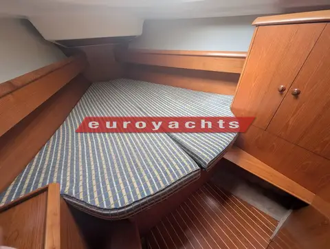 Jeanneau Sun Odyssey 37 Legende: forward cabin V-berth with striped cushions and wooden hanging locker