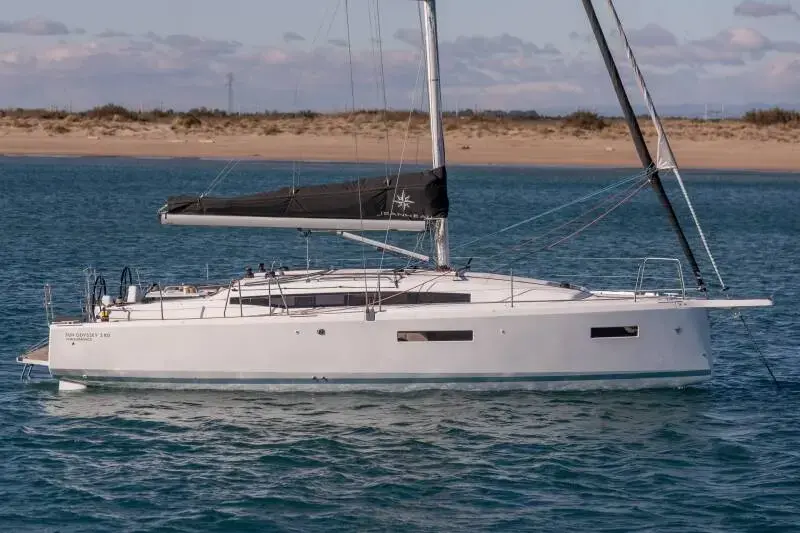 Jeanneau Sun Odyssey 380: white hull at anchor near a sandy shore, mainsail stowed in a dark lazy bag