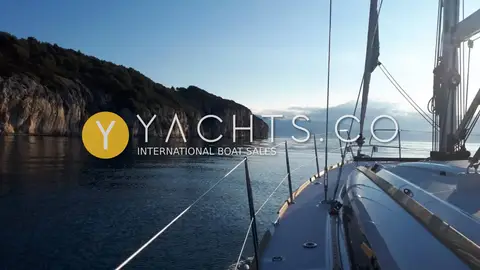Jeanneau Sun Odyssey 389: side deck and guardrails at anchor in calm water beside a rocky wooded headland