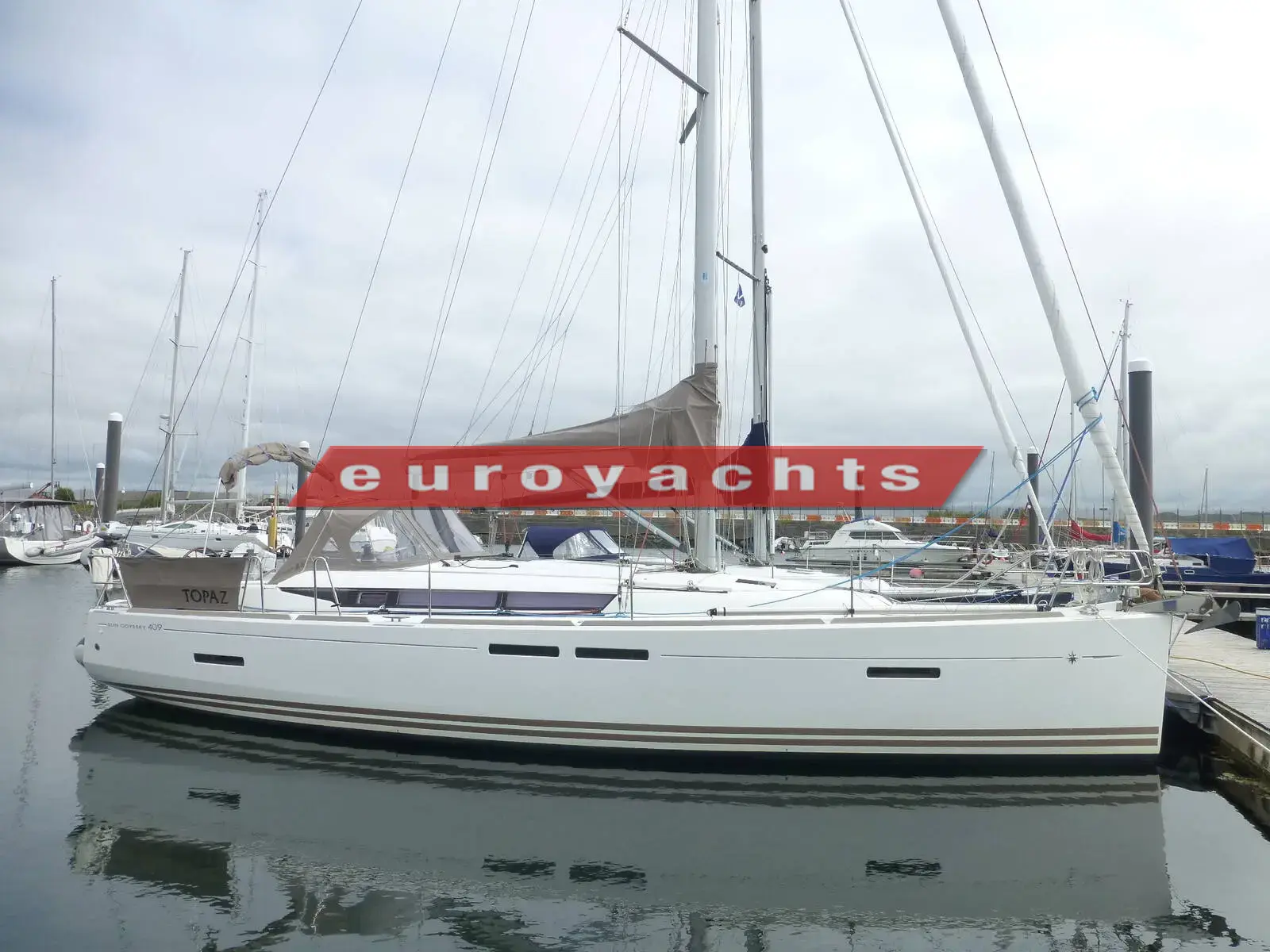 Jeanneau Sun Odyssey 409: starboard side of the white-hulled yacht moored on a marina pontoon, reflected in calm water