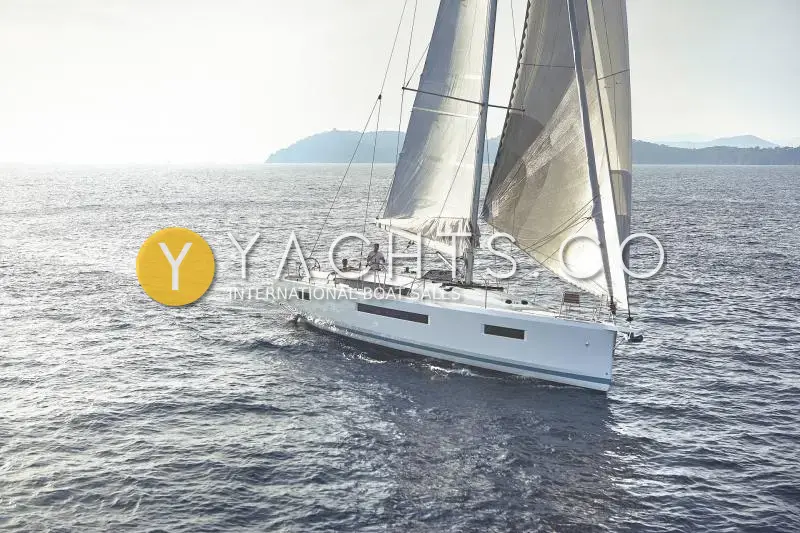 Jeanneau Sun Odyssey 440: white hull under full main and genoa on open sea, headland behind