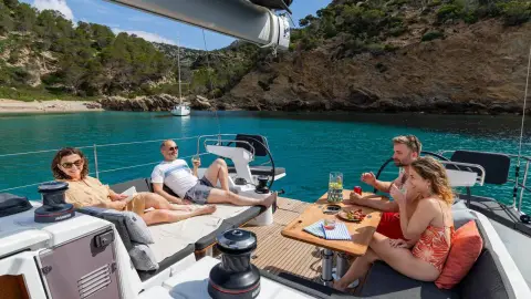 Jeanneau Sun Odyssey 455: cockpit with guests seated around the table, anchored in a rocky wooded bay