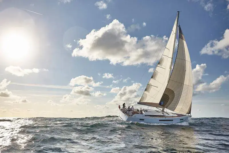 Jeanneau Sun Odyssey 490: sailing upwind under full main and genoa on open sea, sun low behind the sails