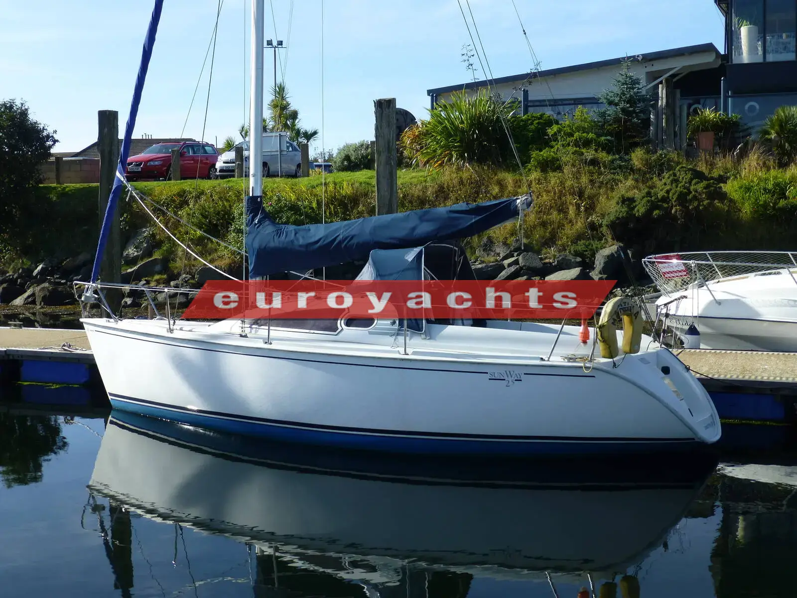 Jeanneau Sunway 25: white hull with blue boot stripe moored in marina, sail cover fitted on boom