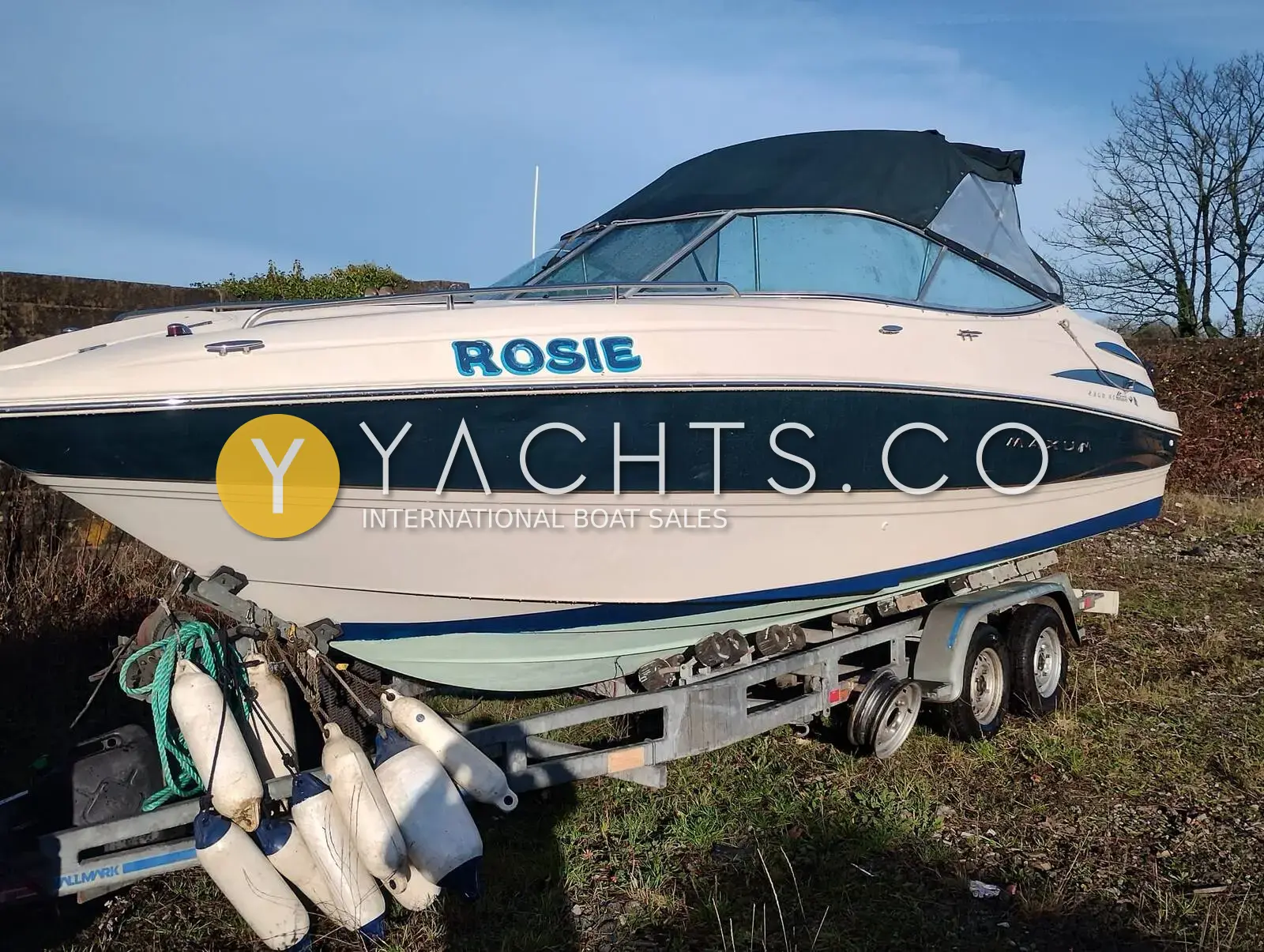 Maxum 2300 SC: bow quarter view of the white and navy hull on her twin-axle trailer, canopy up