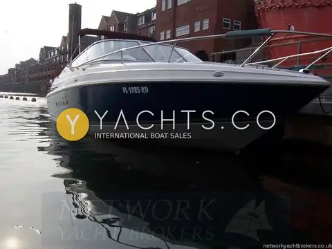Maxum 2300 SC: dark blue hull from the bow quarter, moored beside brick waterfront buildings