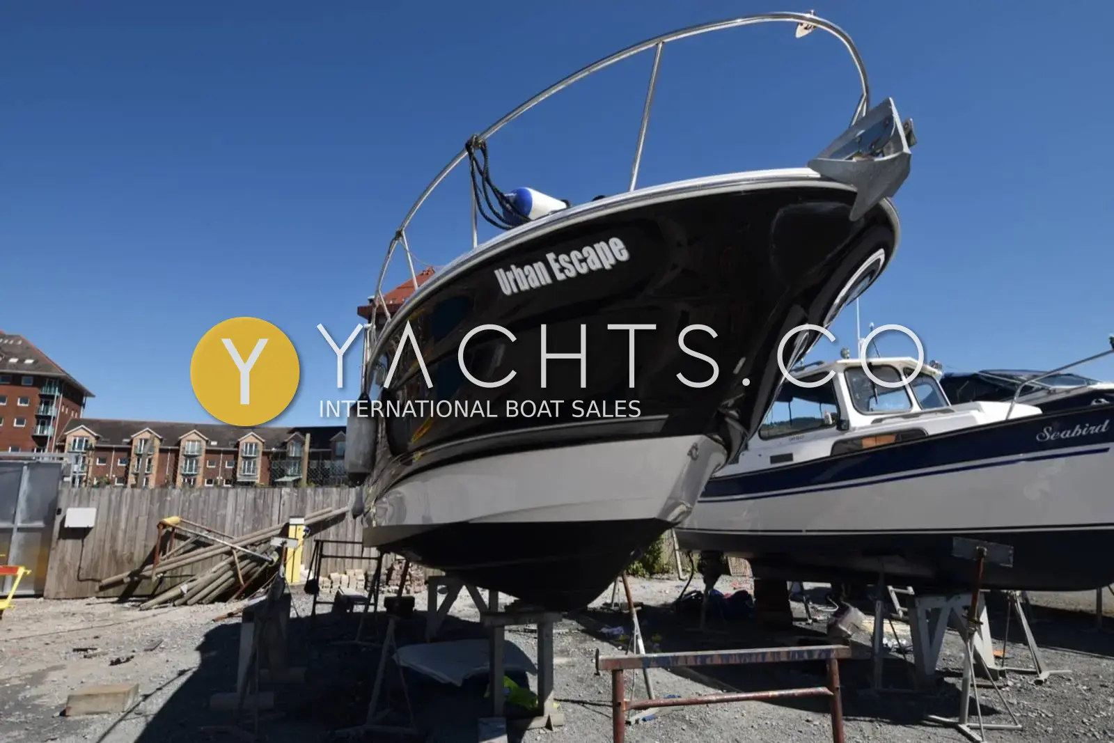 Monterey 245 Sport Cruiser: dark blue bow with Urban Escape lettering and stainless bow rail, ashore on stands in a yard
