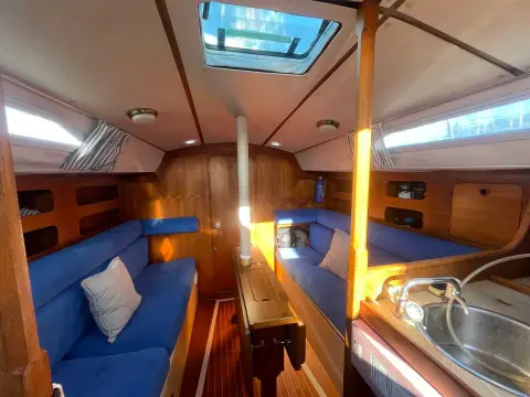 Moody 31: saloon looking forward with blue cushions, wooden joinery, central table and galley sink in foreground