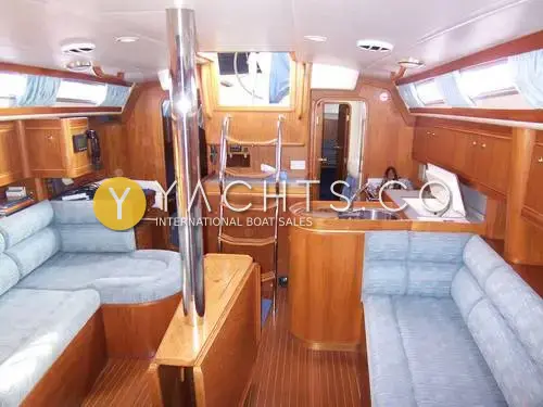 Moody 38CC Yacht For Sale: saloon looking aft, with blue upholstery, teak joinery, companionway steps and galley beyond