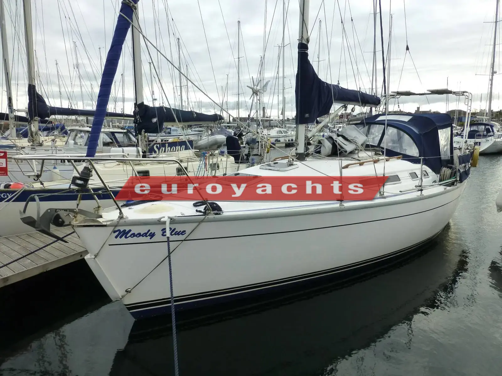 Moody S31: white hull alongside a marina pontoon with blue sprayhood and sail cover fitted