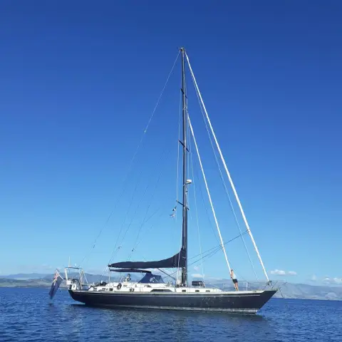 Mystic 60: full profile at anchor showing tall three-spreader mast and navy hull under blue sky