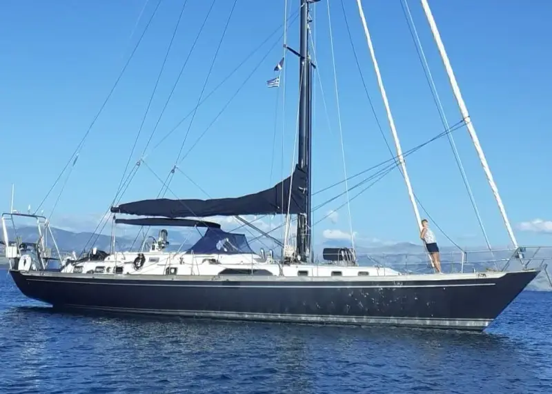 Mystic 60: navy blue hull at anchor off Corfu, sail cover on boom, mountains behind
