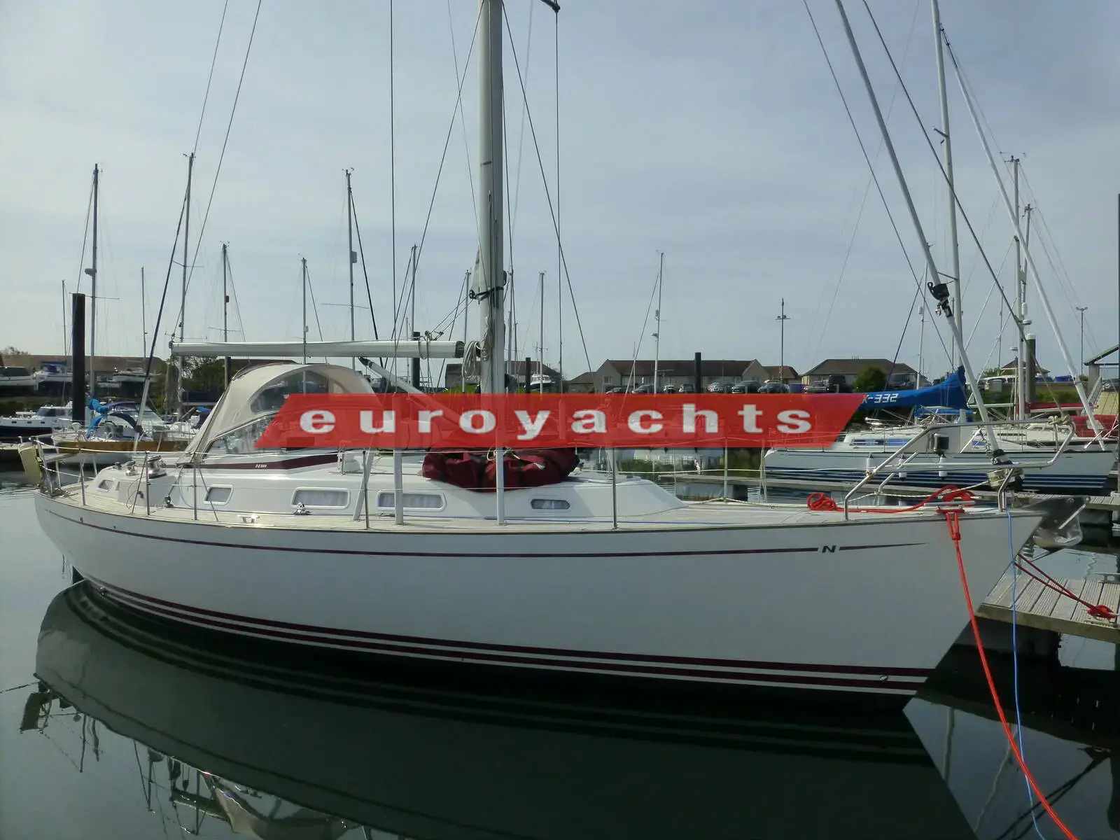 Najad 380: white hull with red trim line afloat in a marina, sprayhood up and mast stepped