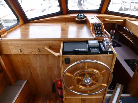 Nauticat 33: inside helm with wooden wheel, plotter and chart table in varnished wheelhouse