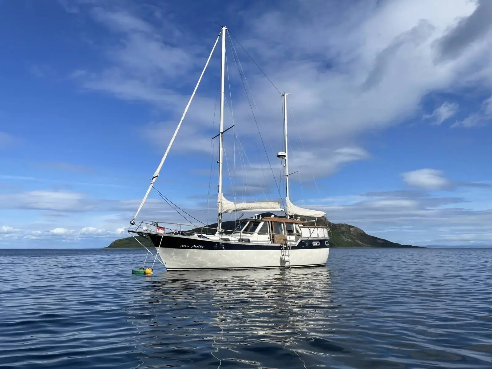Nauticat 33: white ketch at anchor in calm water with headland and blue sky behind
